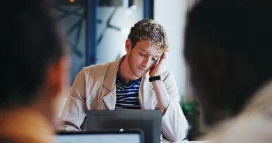 Ung mand sidder foran en computer med haanden til hovedet.