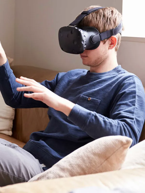 En mand der sidder i en sofa med VR-briller på